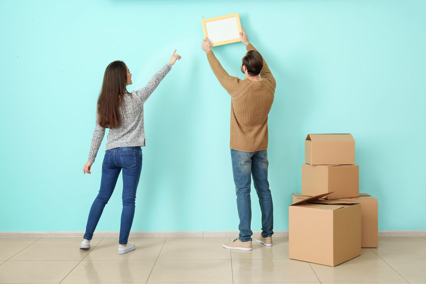 Young couple hanging picture on wall in their new house